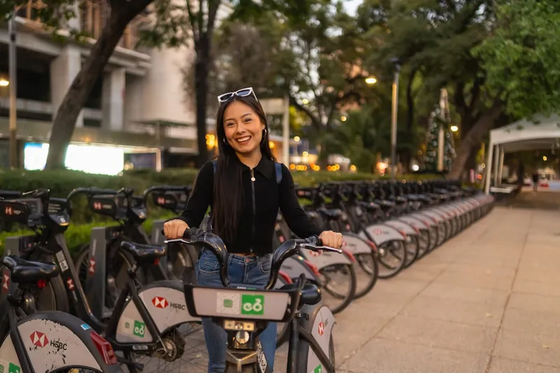 A smiling woman stands by a row of rental bicycles.